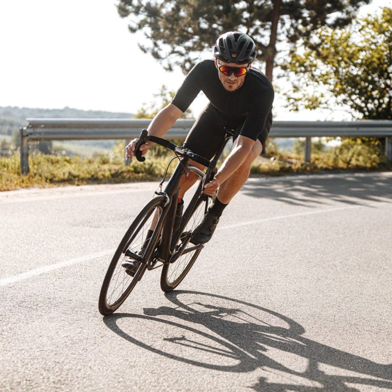 Radfahrer mit Sportbrille fährt schnell auf kurvenreicher Straße.